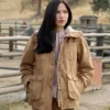 Monica Dutton Yellowstone wearing a brown jacket in an outdoor setting with wooden fences and trees