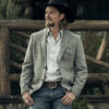 Kayce Dutton wearing a cowboy hat and gray blazer standing in front of a wooden fence.