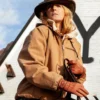 Beth Dutton wearing a brown jacket, hat, and gloves holding a horse bridle against a white wall with a large letter 'Y' Yellowstone Logo
